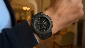 A black dual-display sports watch on a wrist, with a cozy indoor background.